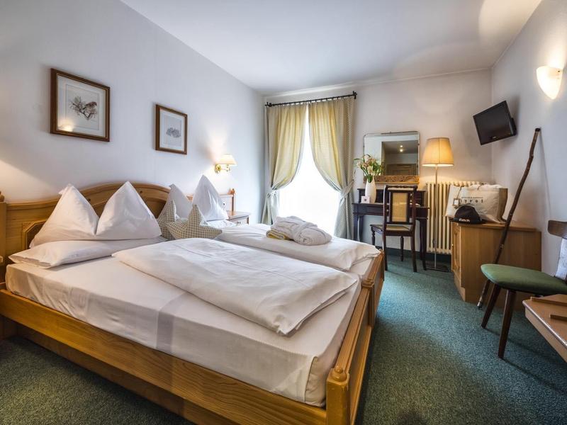 Gemütliches Hotelzimmer mit Doppelbett, Schreibtisch, Fernseher und großem Fenster mit Vorhängen.