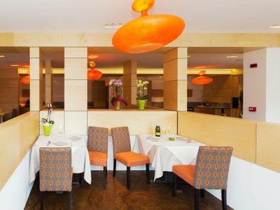 Moderner Essbereich mit weißen Tischen, gemusterten Stühlen und orangen Hängeleuchten.