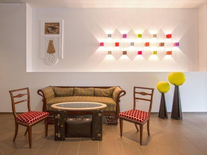 Gemütliche Sitzecke mit Vintage-Sofa, zwei Stühlen, rundem Tisch und Wandregal mit bunten Objekten.