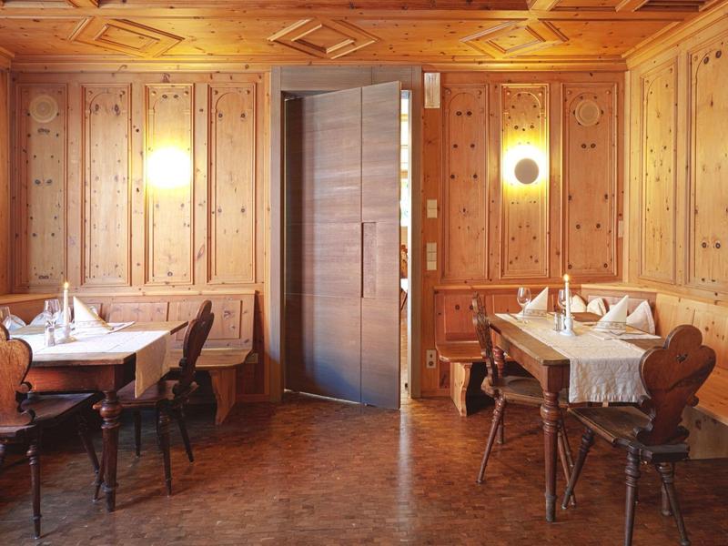 Gemütlicher Raum mit Holzwänden, zwei gedeckten Tischen und warmem Licht an den Wänden.