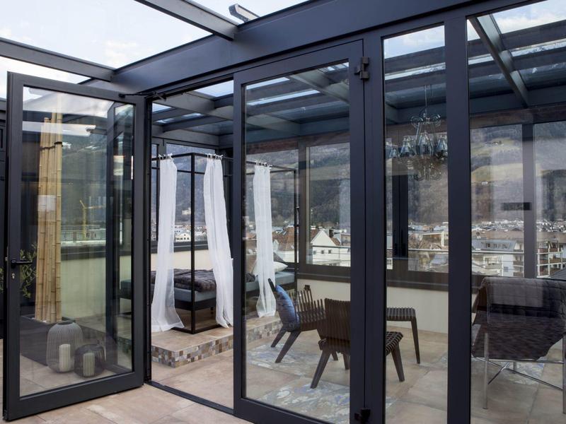 Moderner Wintergarten mit Glaswänden, schwarzem Metallrahmen und gemütlichen Sitzmöbeln innen.