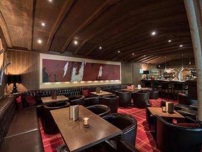 Bar dell'hotel elegante con poltrone in pelle, tavoli in legno e atmosfera calda.