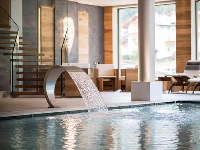 Piscina interna moderna con cascata, pannelli in legno e zone relax.