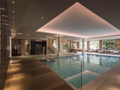 Interno di una piscina coperta moderna e elegante con illuminazione indiretta a soffitto e pavimento in legno.
