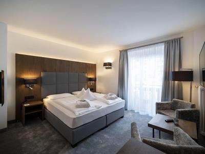 Camera d'hotel moderna con letto matrimoniale, zona salotto e ampia finestra con tende