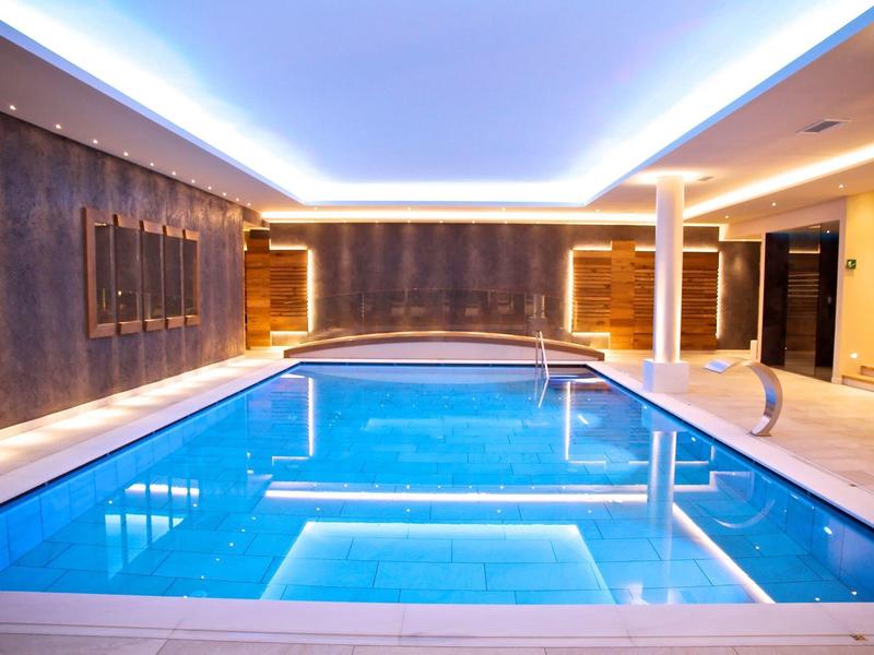 Piscina coperta illuminata con illuminazione moderna al soffitto e pareti eleganti in un hotel.