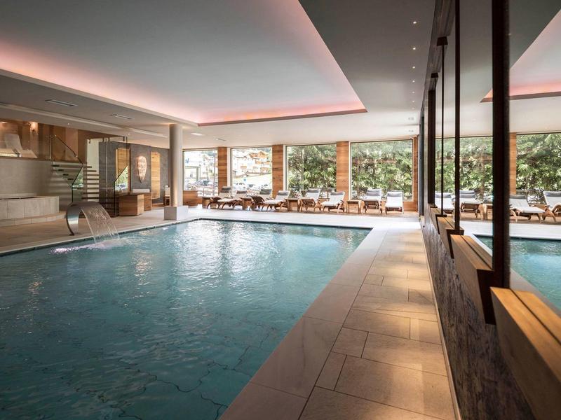 Piscina interna moderna con grandi finestre e lettini accanto all'acqua.