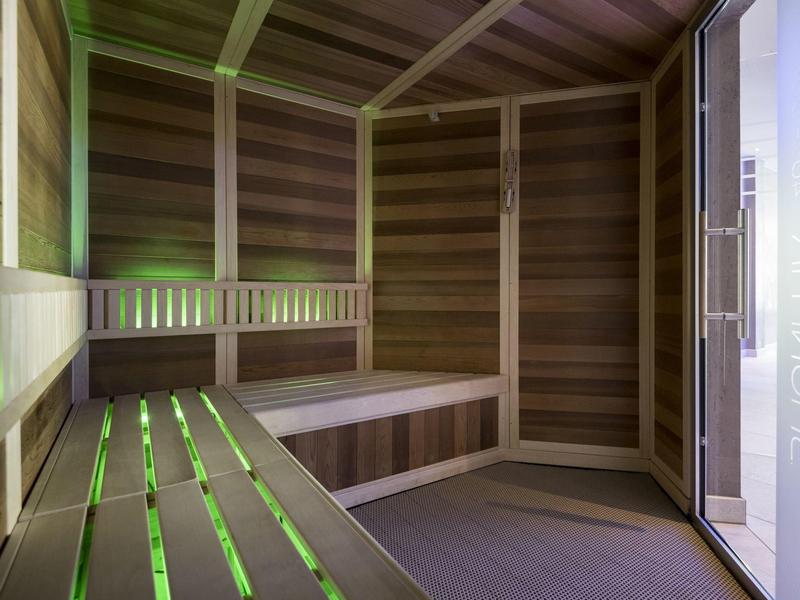 Una sauna moderna con pannelli in legno e illuminazione LED verde sulle panche.