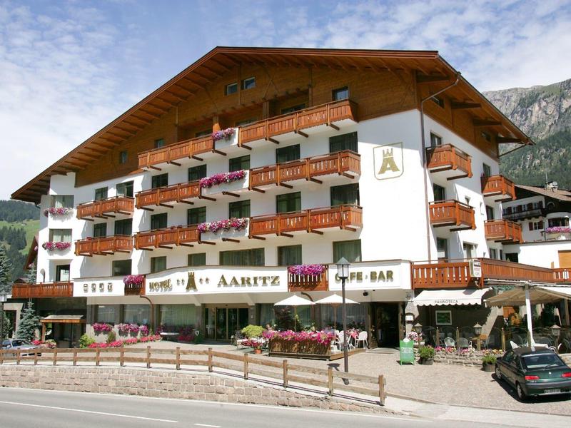 Hotel alpino tradizionale con balconi in legno, fiori e sfondo montano