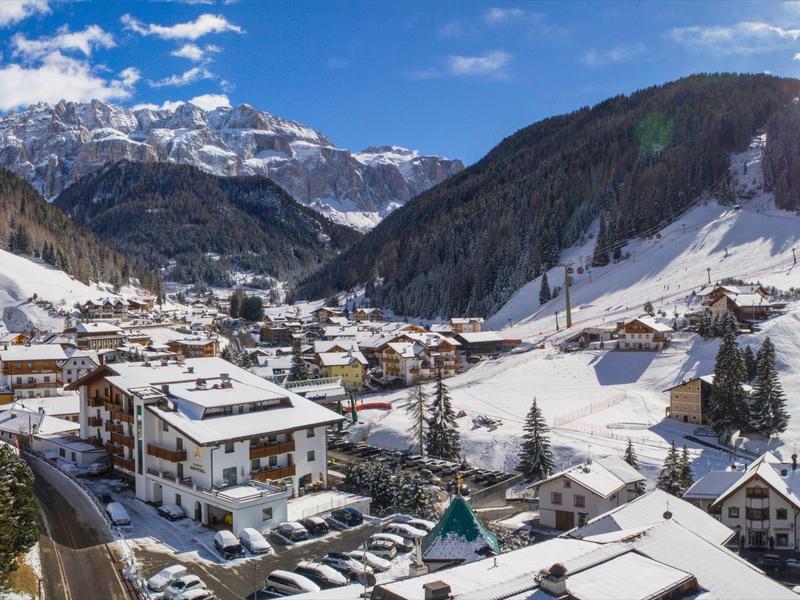 Villaggio di montagna innevato con case, parcheggi e montagne innevate sullo sfondo.