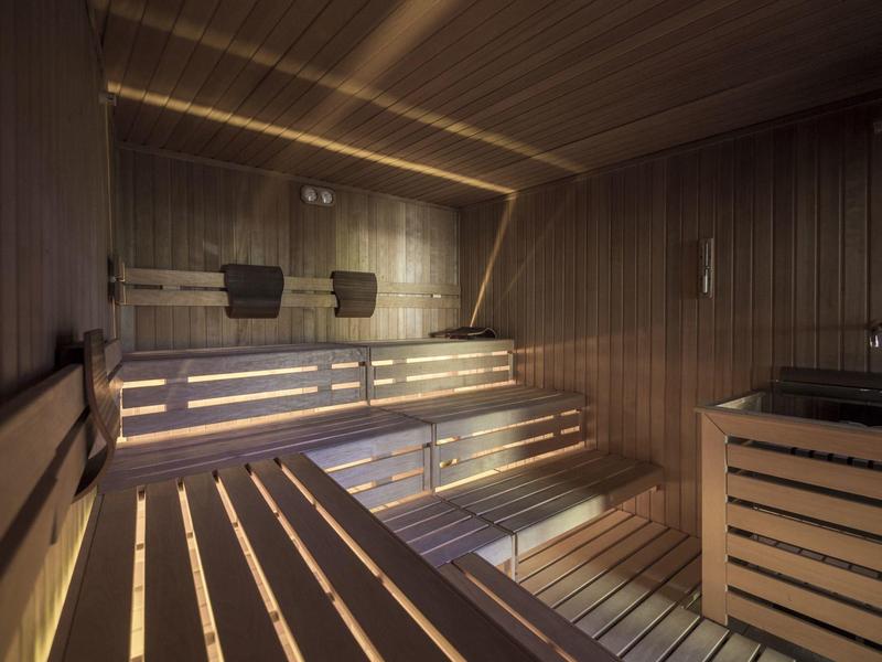 Area sauna con panche in legno su più livelli e illuminazione indiretta.