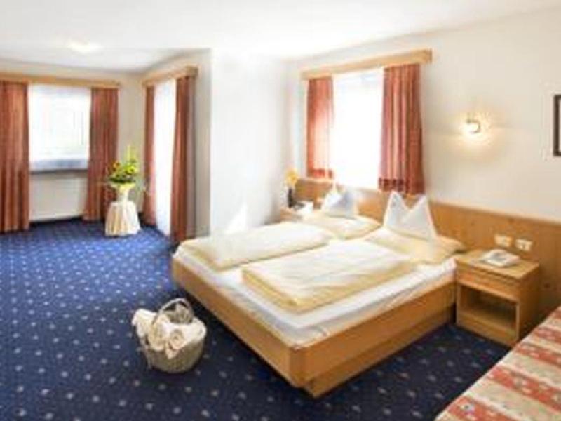 Bright hotel room with double bed, blue carpet, and TV on the desk.