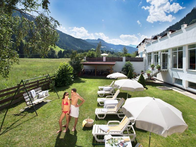 Hotel garden with lounge chairs, umbrellas, and mountain view on a sunny day.