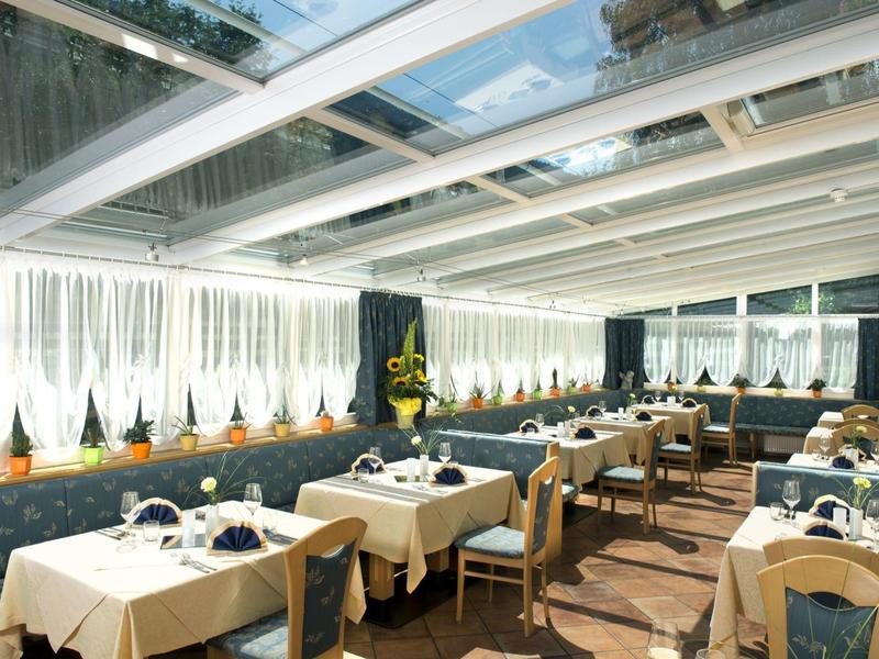 Bright dining area with set tables and chairs under a glass ceiling.