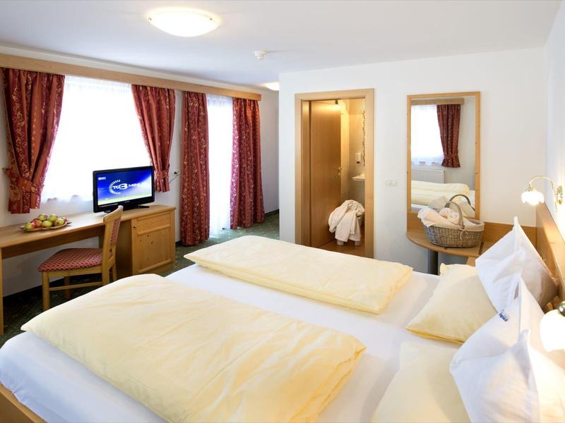 Bright hotel room with two single beds, desk, chairs, and large mirror.