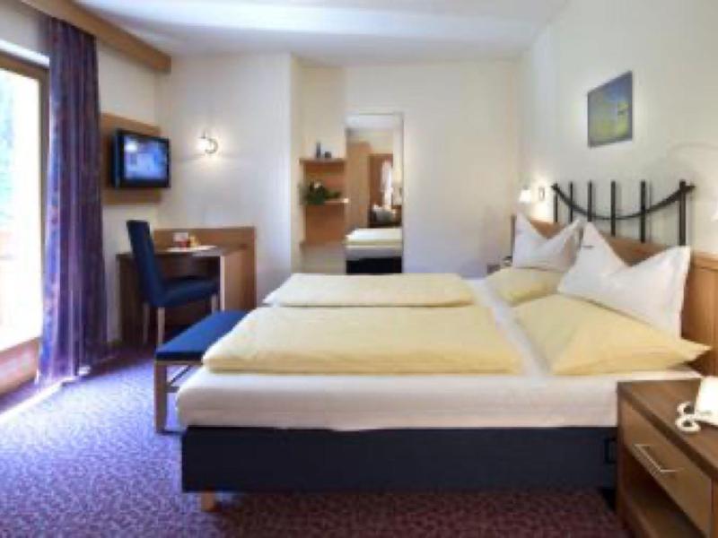 Cozy hotel room with two single beds, desk, and balcony overlooking nature.