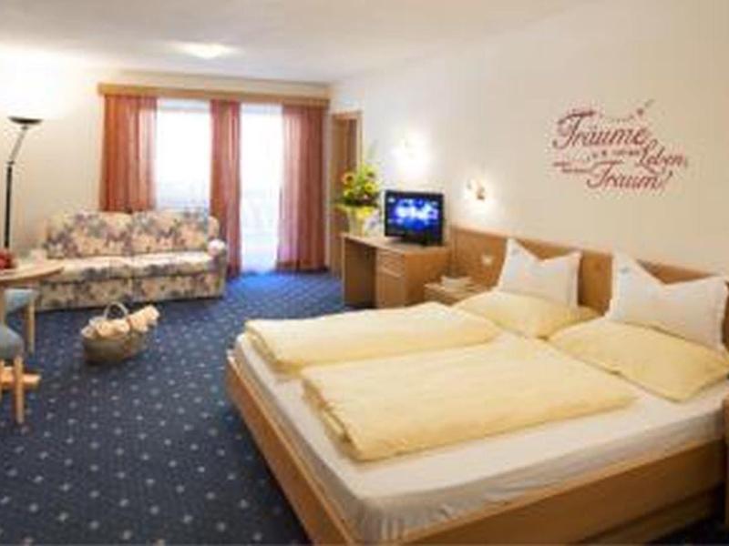 Bright hotel room with two beds, sofa, TV, and carpet flooring.