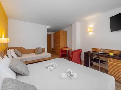 Helles Hotelzimmer mit zwei Betten, Schreibtisch, Fernseher und orangefarbenen Stühlen.