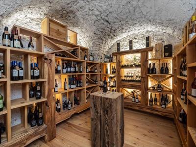 Weinkeller mit Holzregalen und verschiedenen Weinflaschen unter gewölbter Steinmauer.