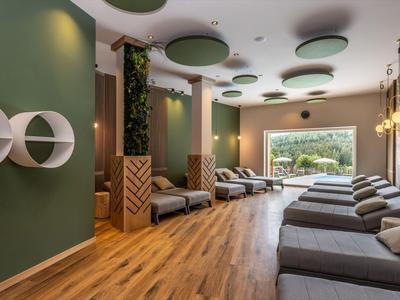 Moderner Wellnessraum mit Liegen, grünen Wänden und großem Fenster mit Blick ins Grüne.