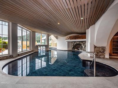 Innenbereich mit einem geschwungenen Schwimmbecken, hohen Fenstern und einer Holzdecke.
