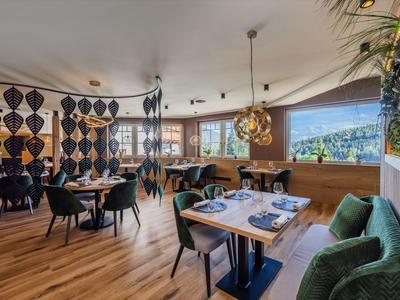Modernes, helles Restaurant mit Holzboden, grünen Stühlen und großen Fenstern mit Aussicht.