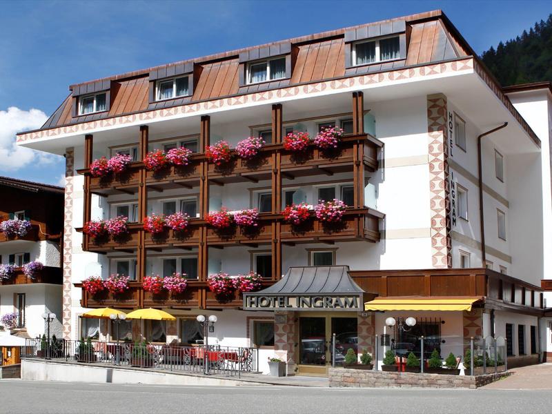 Hôtel à plusieurs étages avec balcons décorés de fleurs devant un arrière-plan montagneux boisée