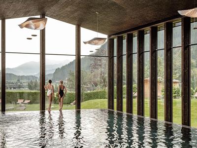 Indoor pool with large glass windows overlooking green mountains and two people by the poolside.