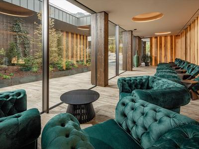 Modern lounge with green velvet armchairs and large windows overlooking an inner courtyard.