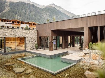 Moderní hotel s venkovním bazénem a výhledem na hory, obklopený přírodou a skalami.