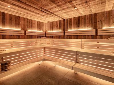 Světlá sauna s dřevěnými lavicemi, teplým osvětlením a dřevěným vědrem na podlaze.