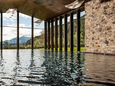 Vnitřní bazén s kamennou zdí a velkými skleněnými okny s výhledem na hory