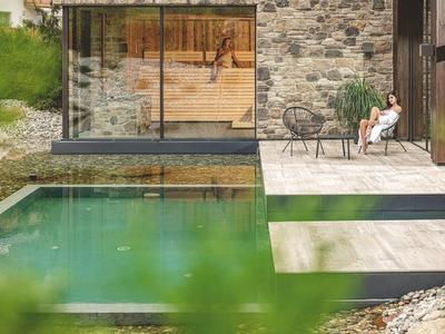 Moderní venkovní prostor s bazénem, terasou a posezením před domem z kamene a skla