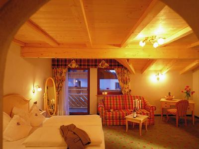 Útulný hotelový pokoj s manželskou postelí, pohovkou, psacím stolem a teplým osvětlením.