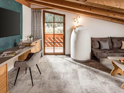 Pohodlný hotelový pokoj se šikmým stropem, pohovkou, psacím stolem a přístupem na balkon.