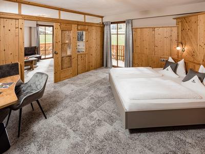 Moderní hotelový pokoj se dřevěným obložením, velkou postelí, psacím stolem a vstupem na balkon