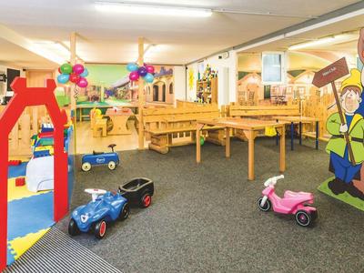 Dětský hrací kout s dřevěným posezením a barevnými hračkami v hotelovém pokoji.