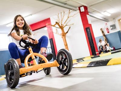 Mladá dívka jezdí na šlapacím vozítku v světlé, moderní vnitřní herně.