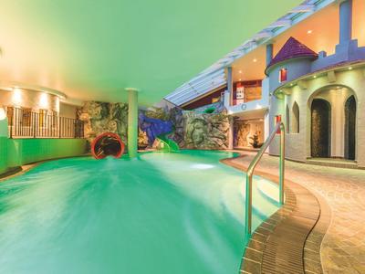 Vnitřní hotelový bazén s vodopádem a kulatými dekoracemi na zdech ve stylu hradu.