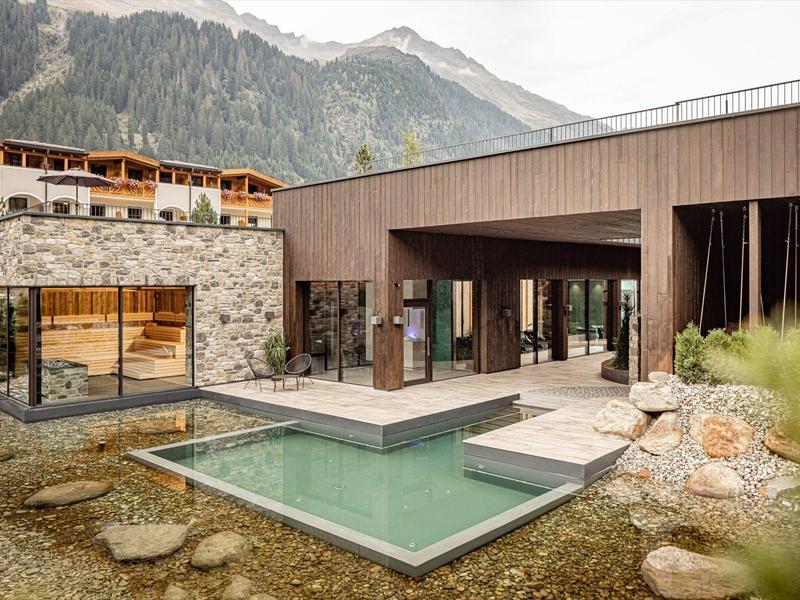 Moderní hotel s venkovním bazénem a výhledem na hory, obklopený přírodou a skalami.