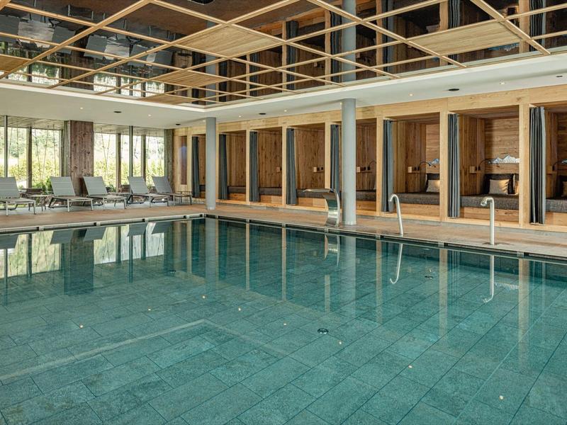 Moderní vnitřní bazén s lehátky a skleněným stropem v hotelu