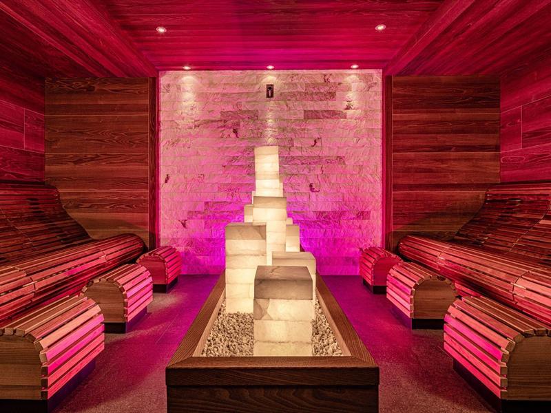 Interiér sauny s dřevěnými lavicemi a světlou kamennou sochou, teplé osvětlení