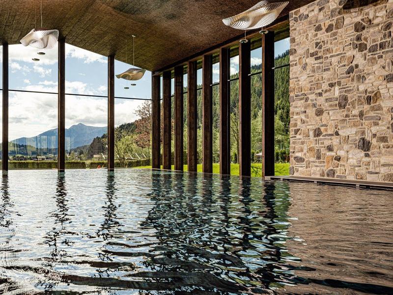 Vnitřní bazén s kamennou zdí a velkými skleněnými okny s výhledem na hory