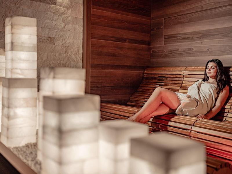 Žena relaxuje v elegantní dřevěné sauně se svítícími sloupy.