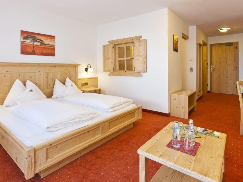 Světlý hotelový pokoj s manželskou postelí, dřevěným nábytkem a červeným kobercem.