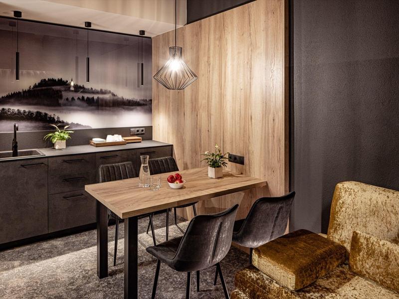 Moderní jídelní prostor s dřevěným stolem, černými židlemi a nástěnným uměním za teplého osvětlení.