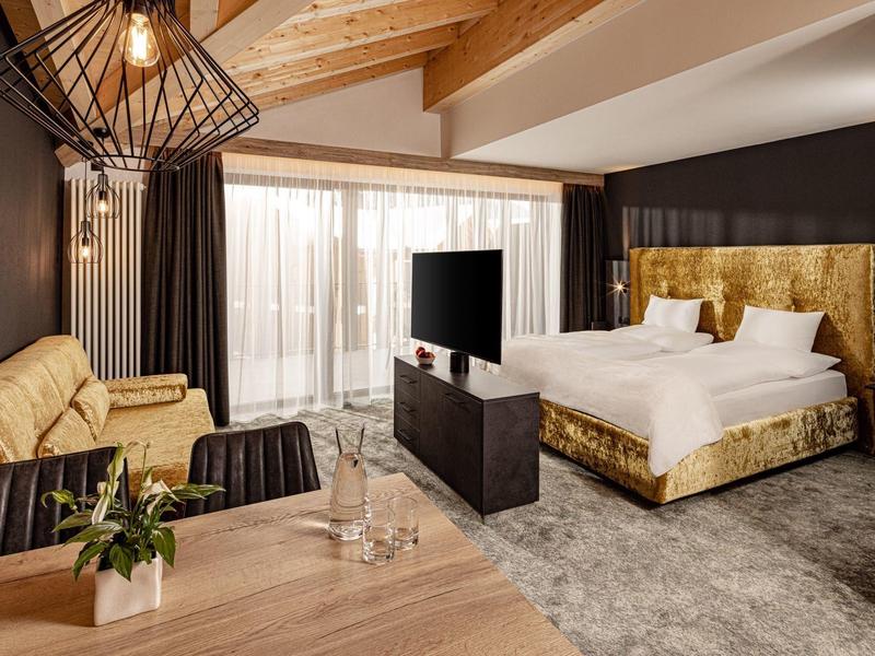 Moderně zařízený hotelový pokoj s velkou postelí, pohovkou a televizí před velkým oknem