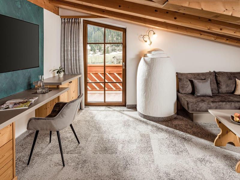 Pohodlný hotelový pokoj se šikmým stropem, pohovkou, psacím stolem a přístupem na balkon.