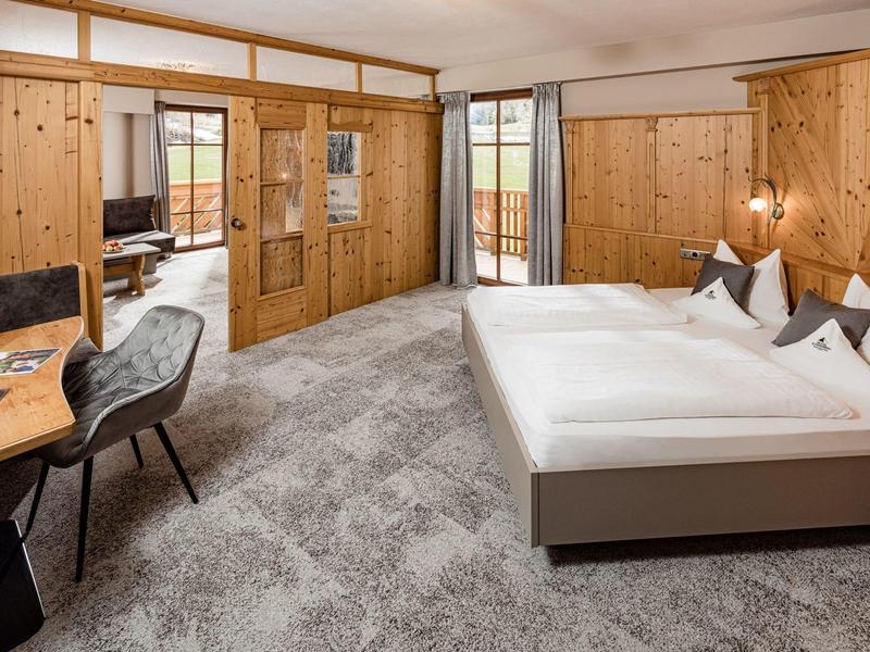 Moderní hotelový pokoj se dřevěným obložením, velkou postelí, psacím stolem a vstupem na balkon