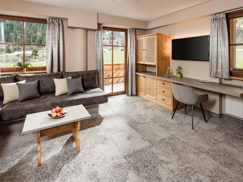 Pohodlný obývací pokoj s pohovkou, konferenčním stolkem, psacím stolem a televizí v hotelovém pokoji.